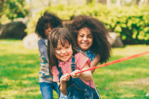 Happy children playing tug of war and having fun during summer camping in the park. Children recreation concept.