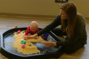 baby playing with cereal in a sand box