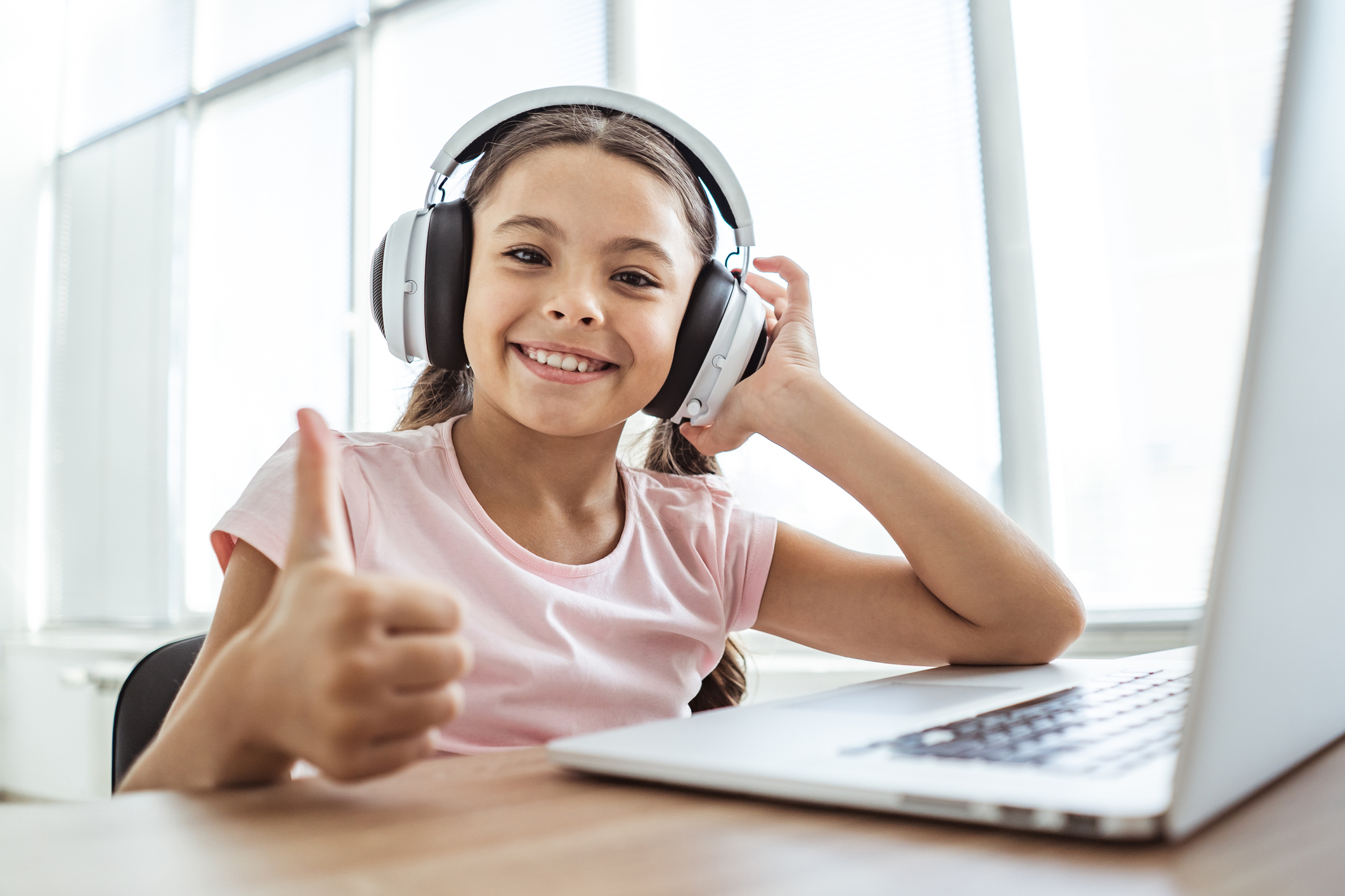 The happy girl in headphones with a laptop thumbs up at the table The happy girl in headphones with a laptop thumbs up at the table