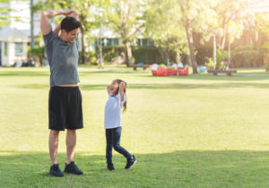 Asian father and his daughter stretching their arms and shoulders before exercising. Workouts and lifestyles concept. Happy family life and Health care concepts. Nature and Outdoors. Kid and dad having Fun with sport day.