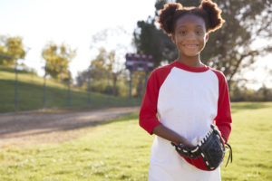 Young Black girl holding baseball mitt smiling to camera