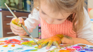 Blonde little girl painting while using her hands to trace 