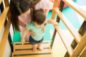 Young woman working as a therapist helping a baby girl go up the stairs in a children therapy center