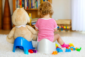 Closeup of 12 months old toddler baby girl child sitting on potty. Kid playing with big plush soft toy. Toilet training concept.
