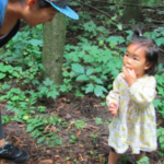 An adult and a young child in a forest. The child is eating berries.