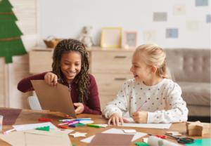 two girls sitting at a table doing crafts with paper