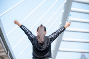 girl standing with her hands in the air holding a water bottle