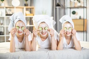 Three teens with facemasks on holding cucumbers over their eyes
