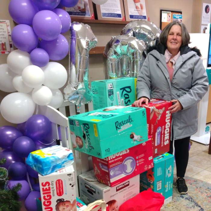 9 A woman smiling next to a large donation of diapers, purple and white balloons in the background