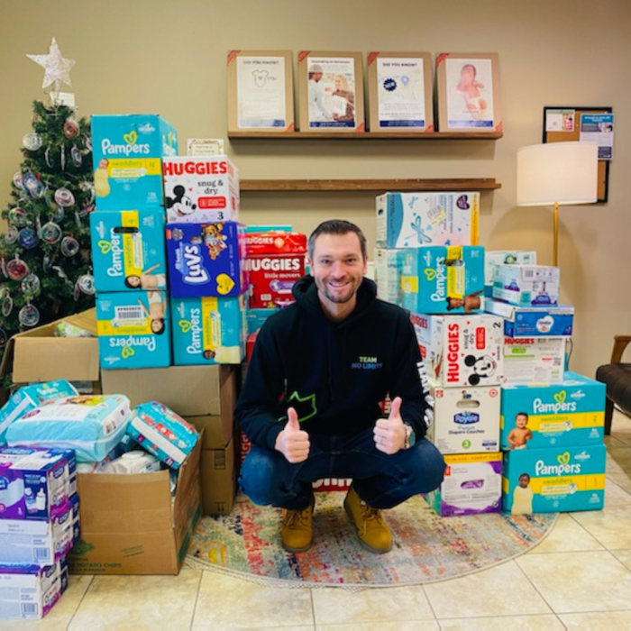 Thursday Jan 2nd (3) A smiling man crouching and giving 2 thumbs up in front of a large donation of diapers