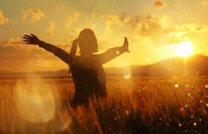 A person standing in a field bathed in sunlight with their arms extended