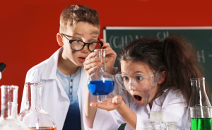 two kids looking at a beaker filled with blue liquid 