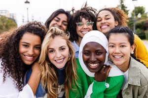 photo of young multiracial girls smiling at camera standing together outdoors. 