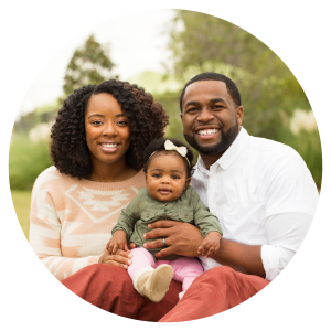 A photo of a mom, dad and baby smiling and looking at the camera in an outdoor setting