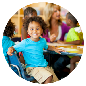 photo of a young child sitting in a chair at a desk smiling at the camera