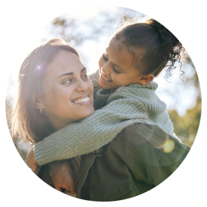 woman carrying child on her back outside. They are looking at each other and smiling